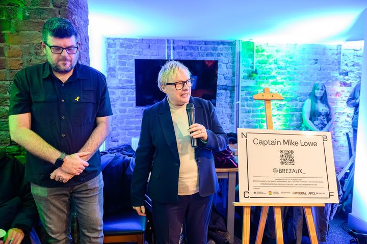 Dame Angela Eagle MP speaking beside the Captain Mike Lowe plaque on its easel, with Rory Wilmer of New Brighton Creative Futures.